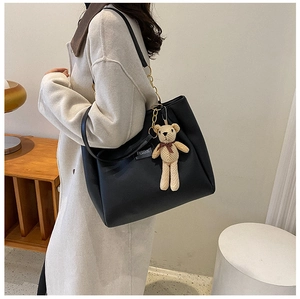 Black leather tote bag with gold chain strap and plush bear charm worn by a model