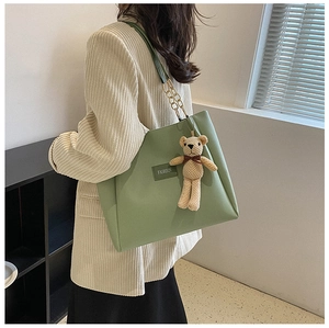 Detail of light green faux leather tote bag with gold chain strap and teddy bear charm