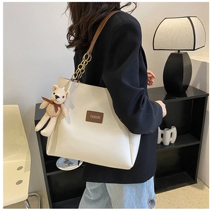 Detail of beige tote bag with chain strap and bear charm worn by a model in casual blazer