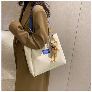 Detail view of large white tote bag with blue leather tag and plush bear charm decoration