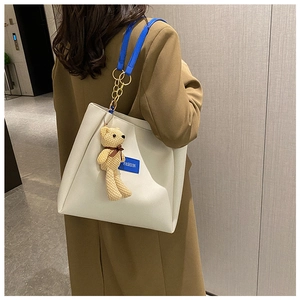 Detail of off-white tote bag with blue shoulder straps and a knitted bear charm