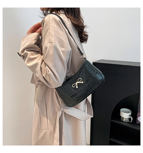Detail of black crocodile embossed shoulder bag featuring a gold bow accent on a model