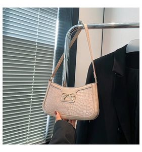 Detail of apricot crocodile texture on shoulder bag with golden metal bow embellishment