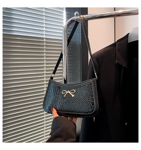 Detail of black faux crocodile skin bag featuring a gold bow buckle and sleek shoulder strap