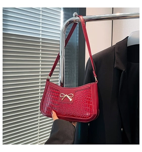 Detail of red faux crocodile leather shoulder bag with a gold metal bow ornament