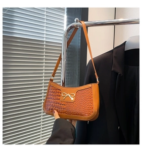 Detail of crocodile pattern texture and golden bow buckle on orange-brown shoulder bag