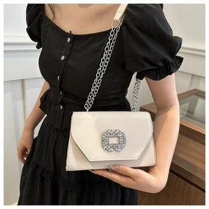 Detail of cream white shoulder bag featuring a sparkling square crystal buckle and silver chain