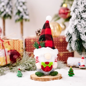 Christmas gnome plush ornament with red plaid hat on a wooden base in festive scene