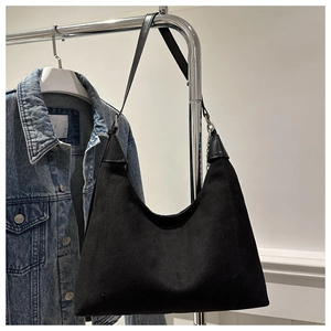Detail of minimalist black hobo bag hanging on metal rack with blue denim background