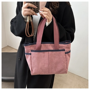 Detail of corduroy tote bag in dusty rose featuring deep blue strap edges and front pockets