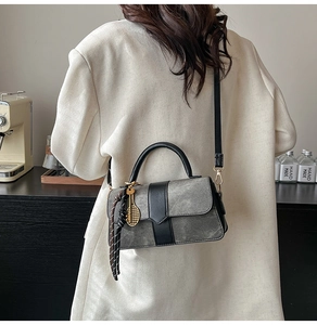 Détail du sac à main gris mat avec garniture en cuir, porte-clés et pompon tressé