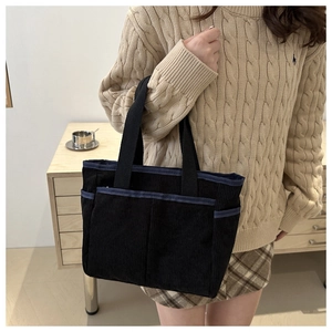 Detail of black corduroy tote bag showing side pockets and navy blue trim on female model