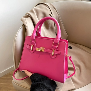 Minimalist bright magenta top handle bag with gold hardware on a beige chair