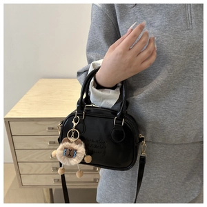 Détail du mini sac Boston en cuir noir avec fermeture éclair dorée et texte embossé