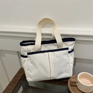 White corduroy tote bag with blue trim and large pockets on a wooden table setup