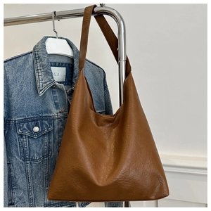 Detail of vintage brown tote bag with leather texture hanging by a blue denim jacket