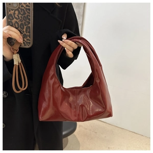 Close-up of a burgundy glossy hobo bag held by a model in a black winter coat