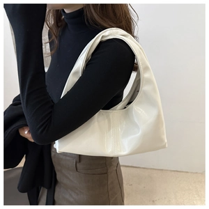 Close-up of a white patent leather hobo bag worn by a model in a minimalist setting