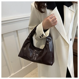 Chic dark brown crescent hobo bag in glossy patent leather worn over the shoulder