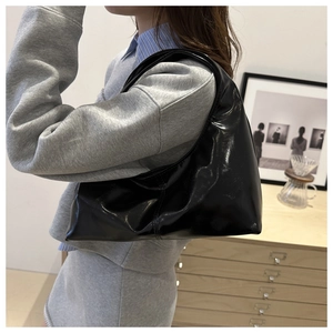 Detail of glossy black patent leather shoulder bag with smooth half-moon shape and stitching