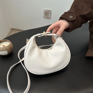 White crocodile-embossed crescent moon bag with gold hardware on a dark background