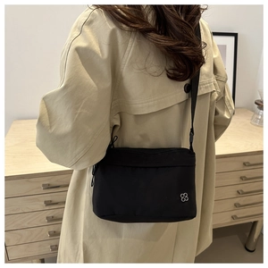 Rear view of a casual black nylon crossbody bag with silver flower logo on a beige trench coat