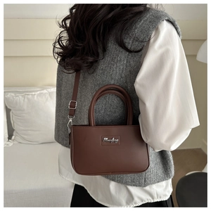 Detailed view of the brown leather crossbody bag with metal logo and adjustable strap