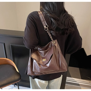 Macro detail of deep brown glossy tote bag with gold chain strap and turn-lock closure