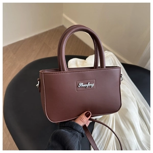 Detail of hand-held minimalist dark brown faux leather crossbody bag with metal logo