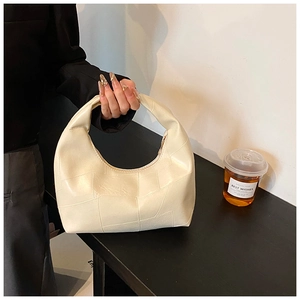 Detail of cream hobo handbag with geometric stitching on a modern wooden surface
