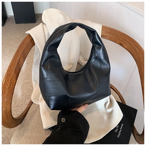 Detailed view of black geometric patchwork leather handbag on a beige garment