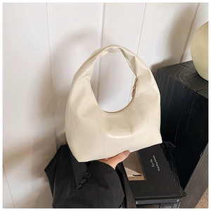Detail of a quilted cream hobo bag with a gold zipper on a minimalist display