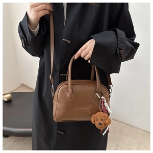 Detail of a brown faux leather Boston bag with embossed logo and cute teddy bear charm