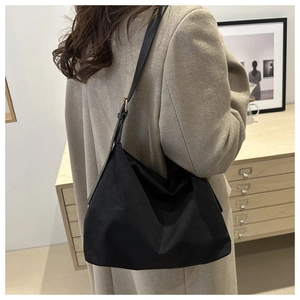 Detailed side view of a minimalist black nylon tote bag on a model in a cozy interior