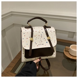 Close-up of a white polka dot backpack with brown trim and rabbit logo on a glass table