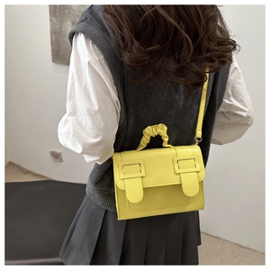 Detail of yellow pleated handle and decorative square buckles on flap crossbody bag
