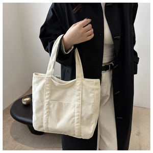Close-up of cream corduroy tote bag with front pocket shown on a female shoulder