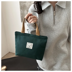 Close-up of a dark green canvas handbag with a bear patch and light brown handles