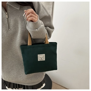 Detail of dark green canvas mini tote with cartoon bear patch and brown handles
