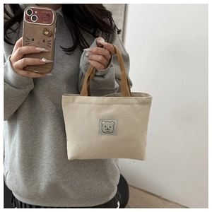 Close-up of a mini canvas bag with brown handles and a cute cartoon bear patch