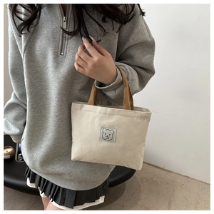 Close-up of cream canvas tote bag with cute bear patch and woven brown handles