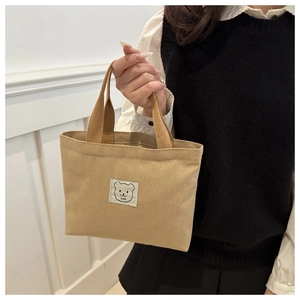 Detail of khaki canvas bucket bag with embroidered cartoon bear patch and LUNE logo strap