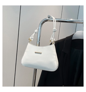 Close-up of white minimalist baguette bag with gold metal clasp and knotted strap detail