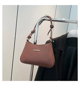 Detail of a brown leather shoulder bag featuring a gold buckle and knotted strap design