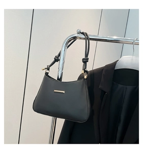 Detail of minimalist black underarm bag with gold metal trim and leather shoulder strap