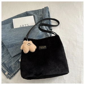 Détail d'un sac bandoulière en peluche noire avec pendentif ours et lettrage doré