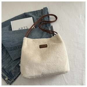 Vue détaillée du sac seau en peluche beige avec étiquette en cuir et fine bandoulière