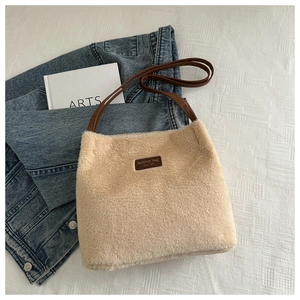 Détail du sac seau en peluche avec lanières en cuir sur un fond blanc minimaliste