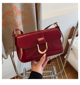 Detail of burgundy patent leather bag with glossy finish and gold U-shaped metal buckle