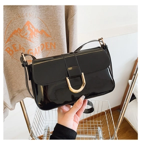 Close-up of shiny black patent leather shoulder bag with vintage gold horseshoe buckle